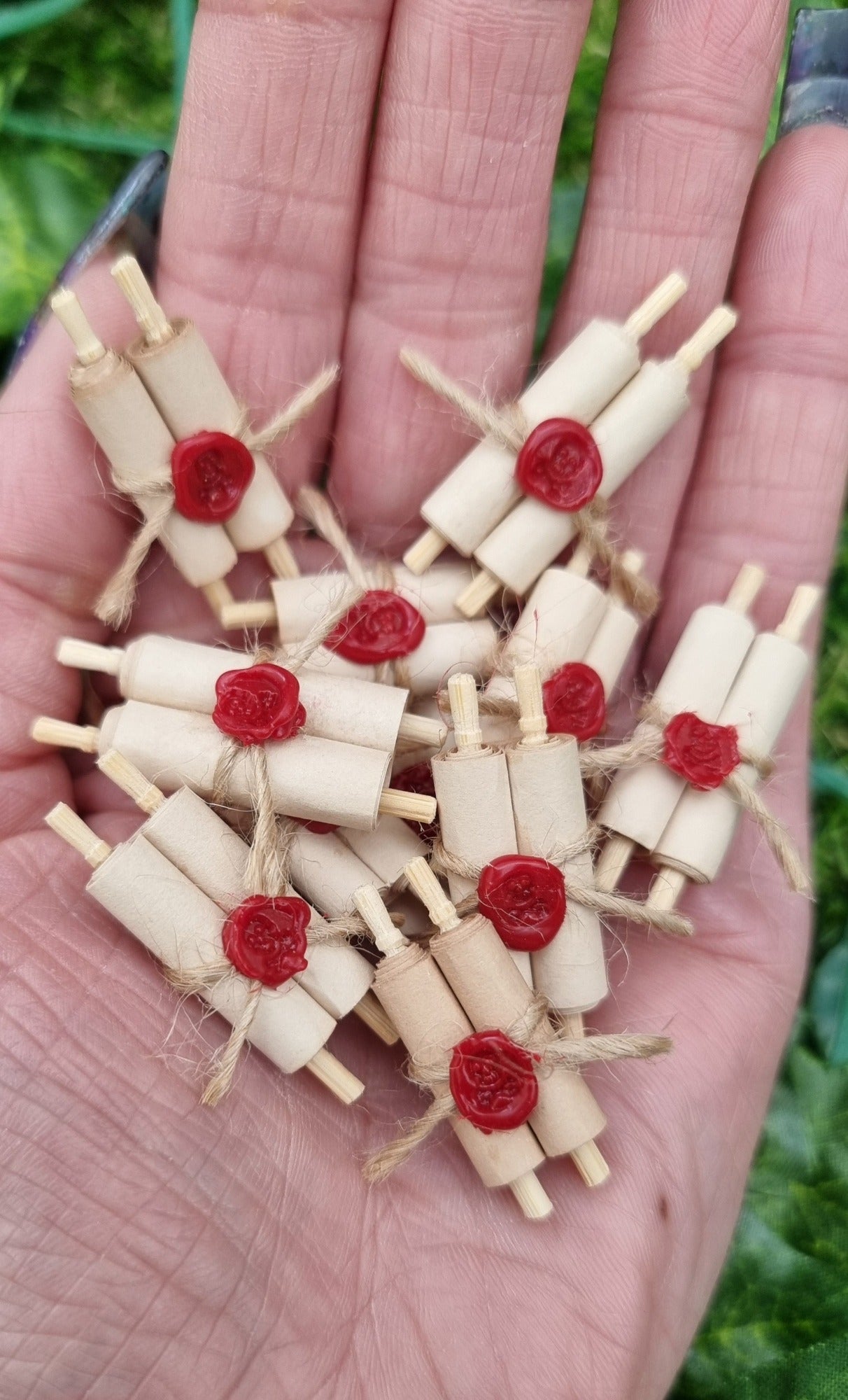 Miniature 1:12 scale double scrolls are held in the palm of a hand. Each scroll has 2 rolls of paper around 2 wooden handles and bound with jute string a wax seal. The wax seal has a skull and crossbones indent