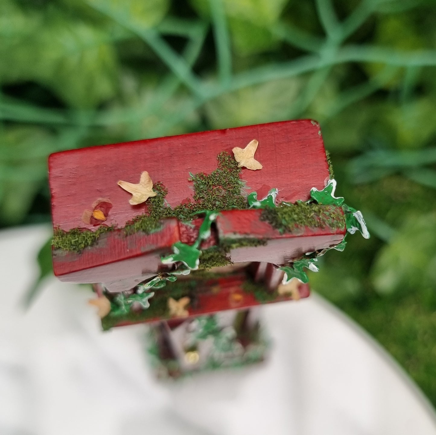 Miniature 1:12 scale grandfather clock sits of a marble slab. Shown from above, the top of the clock has moss, green ivy and dead leaves climbing down to the rest of the clock and moss.