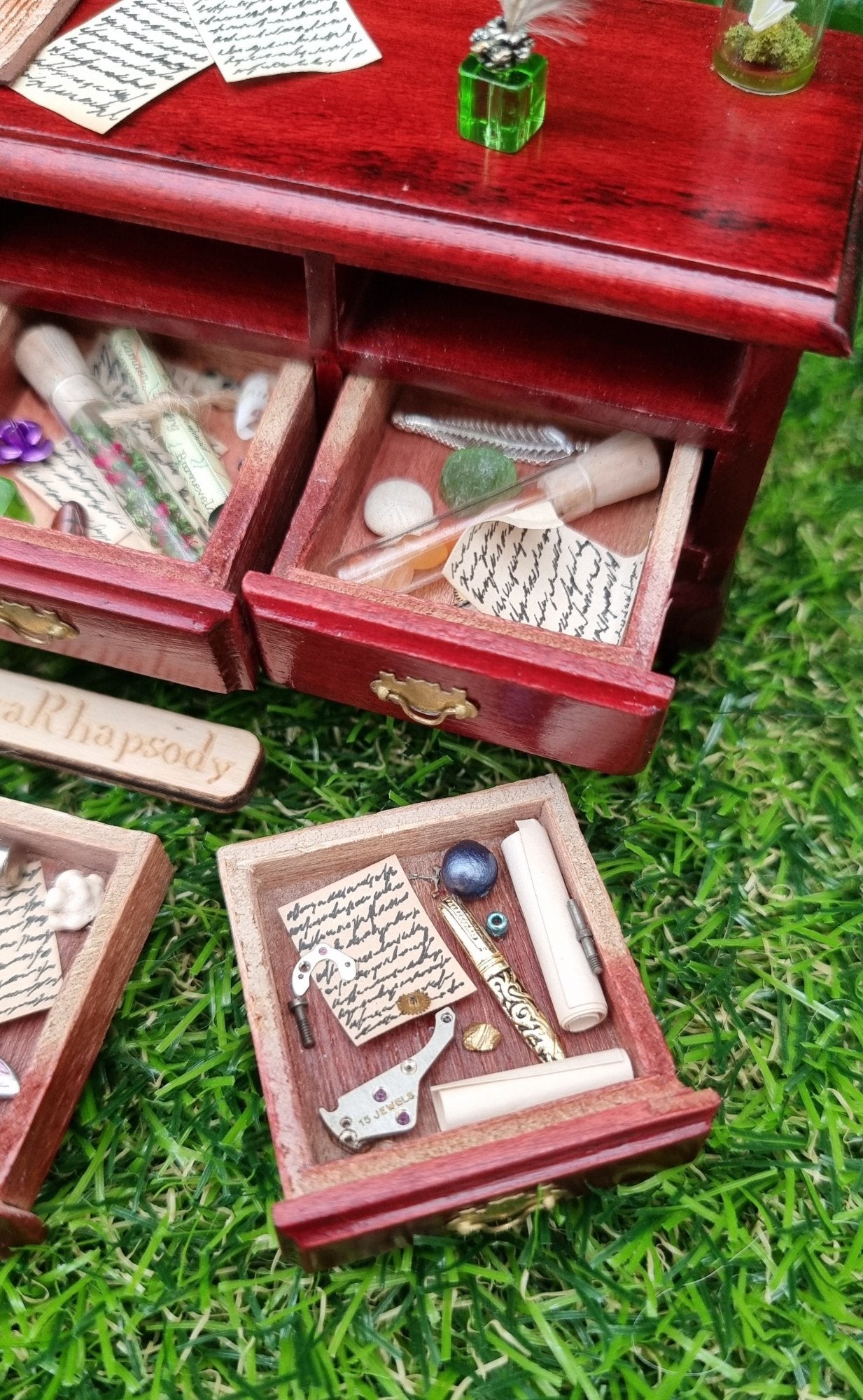 Miniature 1:12 scale dollhouse sideboard showing detail of 2 open drawers, containing bottle, parchments, trinkets and curios. The countertop has parchments, inkwell and butterfly bottle in view