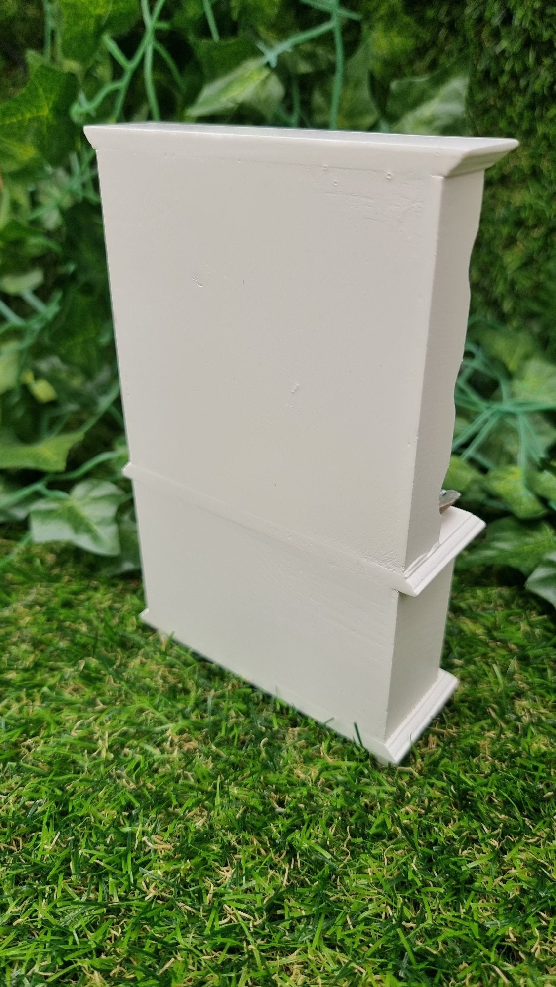 Back of a miniature 1:12 scale white dresser, sitting against a green background.