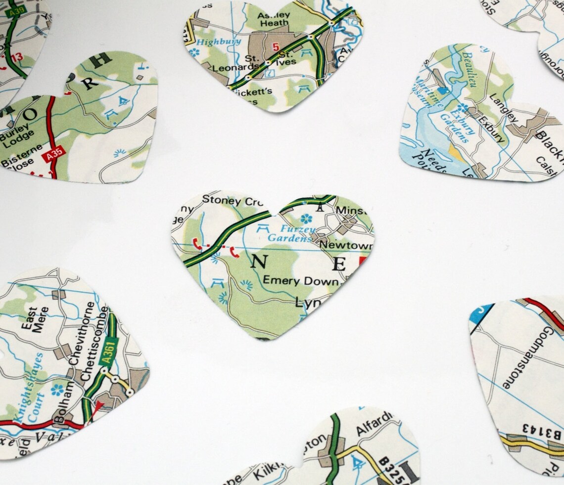 Map paper confetti pieces in heart shapes are scattered on a white background. The paper confetti is primarily white with green, blue and red colours