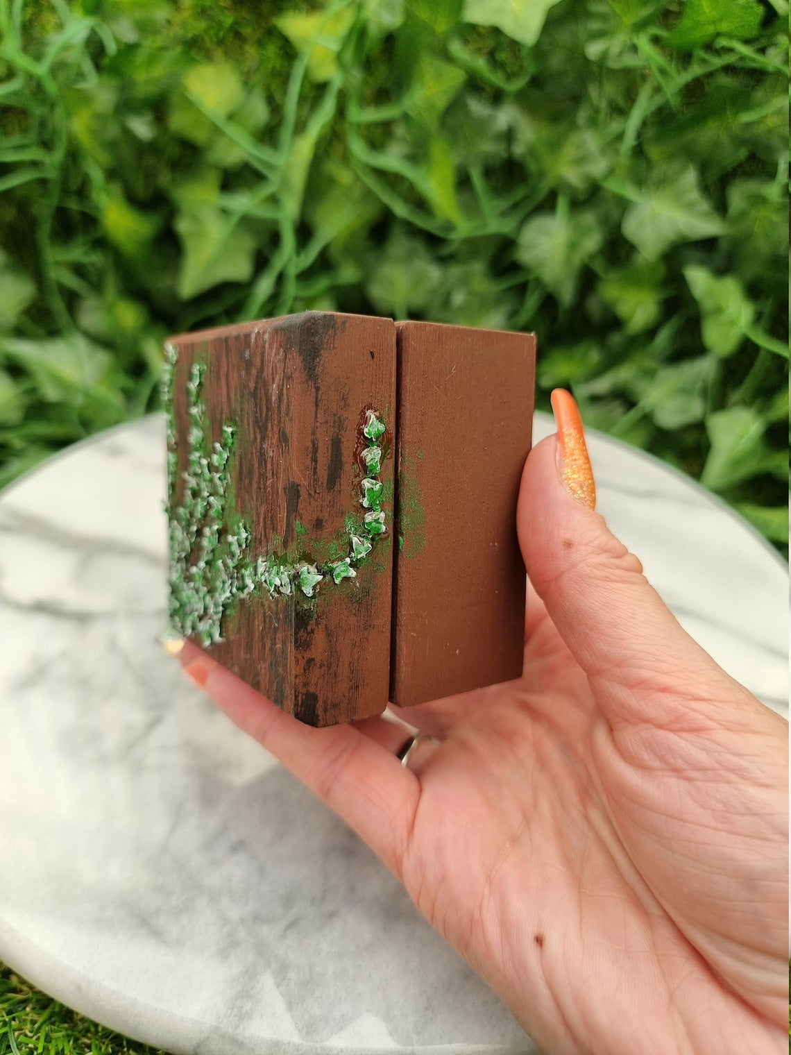 Small painted wooden box held in a hand against a marble background. The box has tiny green ivy leaves creeping across from left to right and around the side of the box