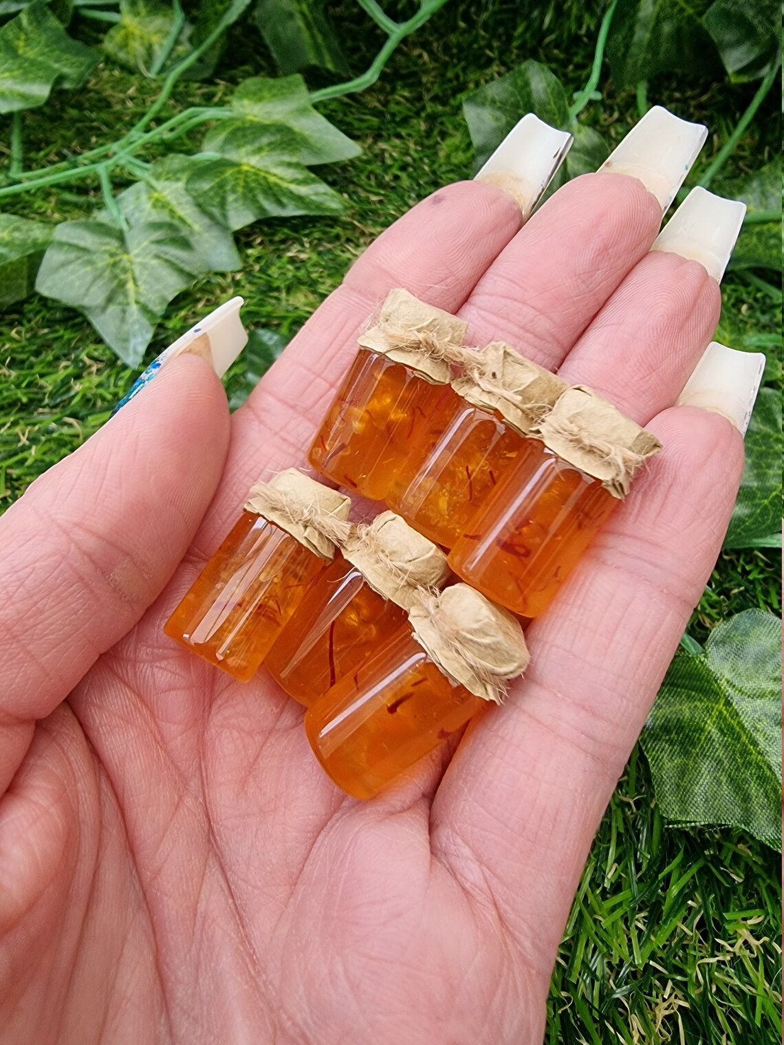 Several miniature jars of shredded orange marmalade with brown paper lids are show held in the palm of a hand against a green background