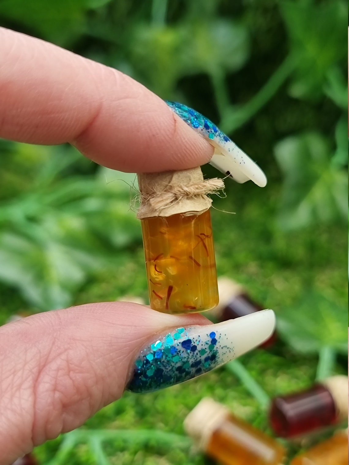 A miniature jar of shredded orange marmalade with a brown paper lid is shown held between a finger and thumb against a green background