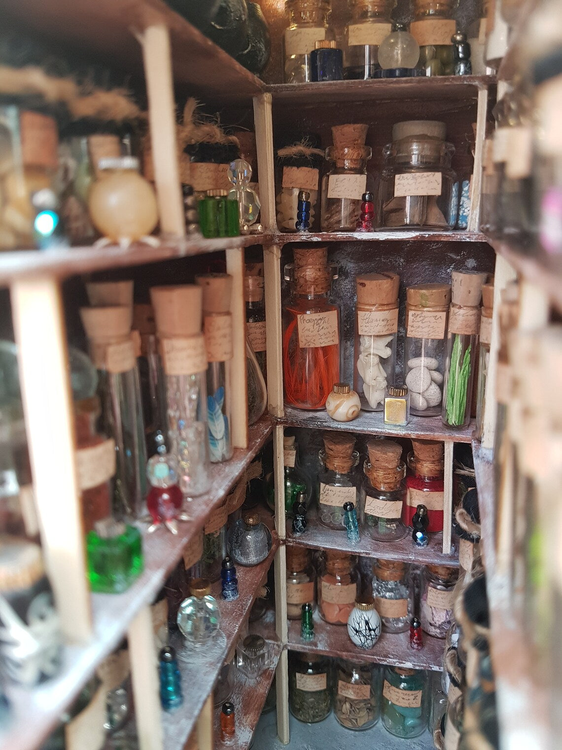 Details shown of the small open fronted book nook shelf insert box. The box contains 5 sets of shelves up to the ceiling on all sides, each full of glass vials and vessels. Each vial has an aged brown label