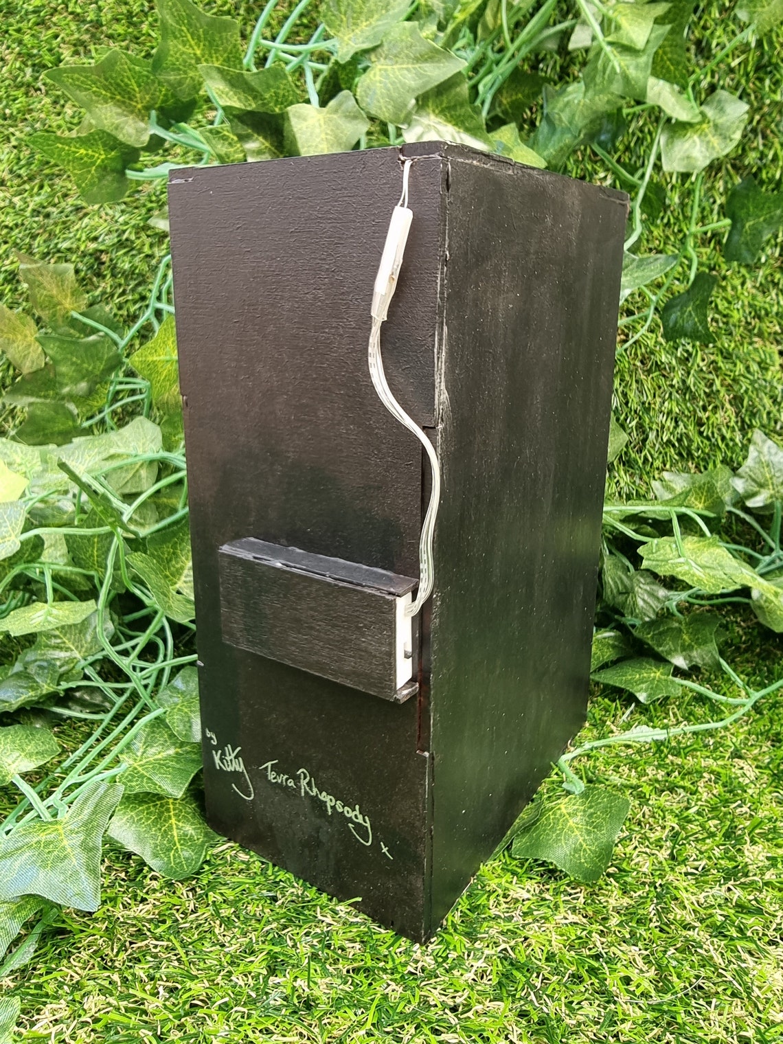 The back of the book nook box is shown. It is black with a small insert for a battery pack coming from the box lid. The box states it is made by Kitty, Terra Rhapsody