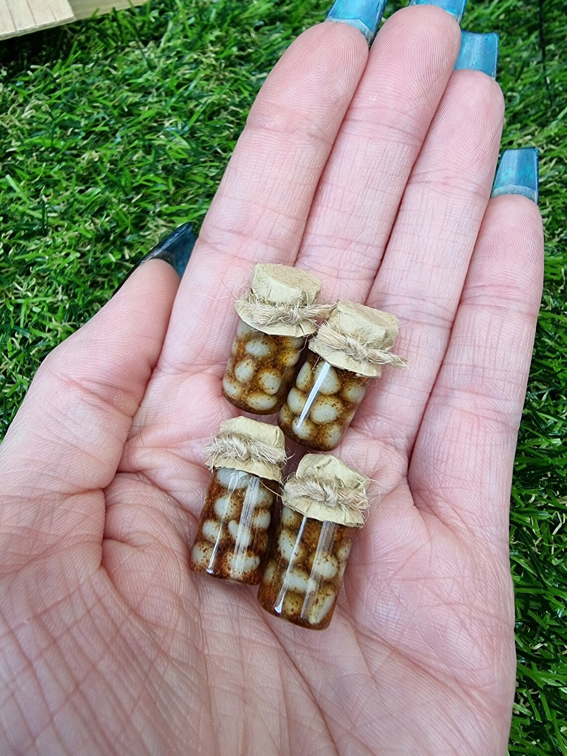 Several 1:12 scale miniature preserve jars with paper lids held in an open palm. Jars contain pickled onions eggs