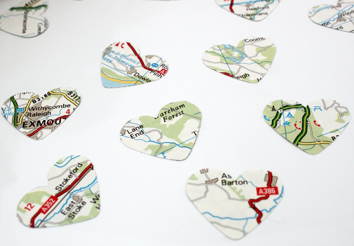 Map paper confetti pieces in heart shapes are scattered on a white background. The paper confetti is primarily white with green, blue and red colours