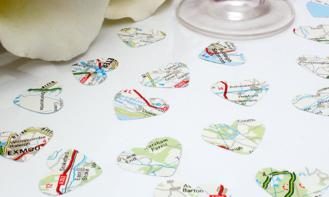 Map paper confetti pieces in heart shapes are scattered on a white background. The paper confetti is primarily white with green, blue and red colours