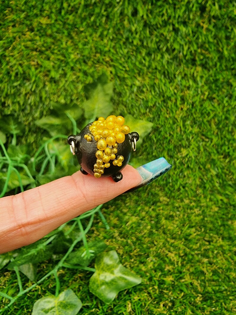 Single miniature black cauldron overflowing with bubbles are displayed on a finger tip. The cauldron is overflowing with gold bubblesSingle miniature black cauldron displayed on a finger tip. The black cauldron is overflowing with silver bubbles