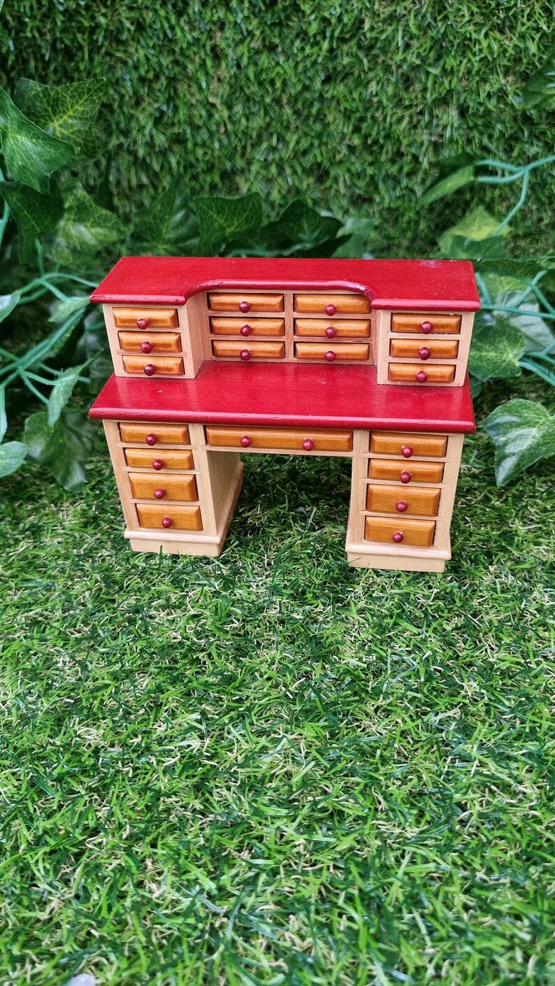 1:12 scale desk with 21 drawers is sat on a green grass backgroundthe desk is like brown with darker brown counter tops. All drawers are closed.