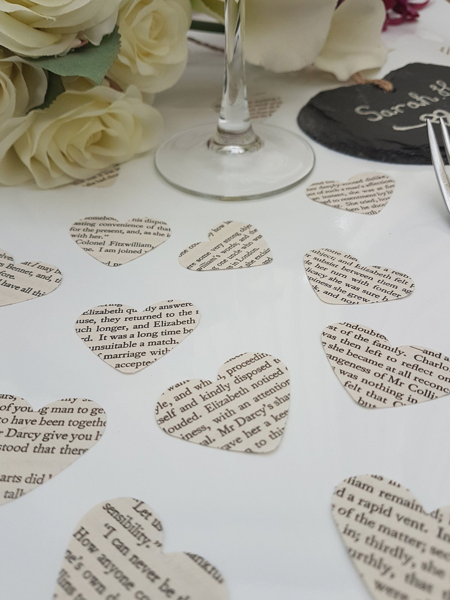 Small cream paper confetti hearts are scattered on a white background. The text displayed on the confetti pieces shows text from Pride and Prejudice