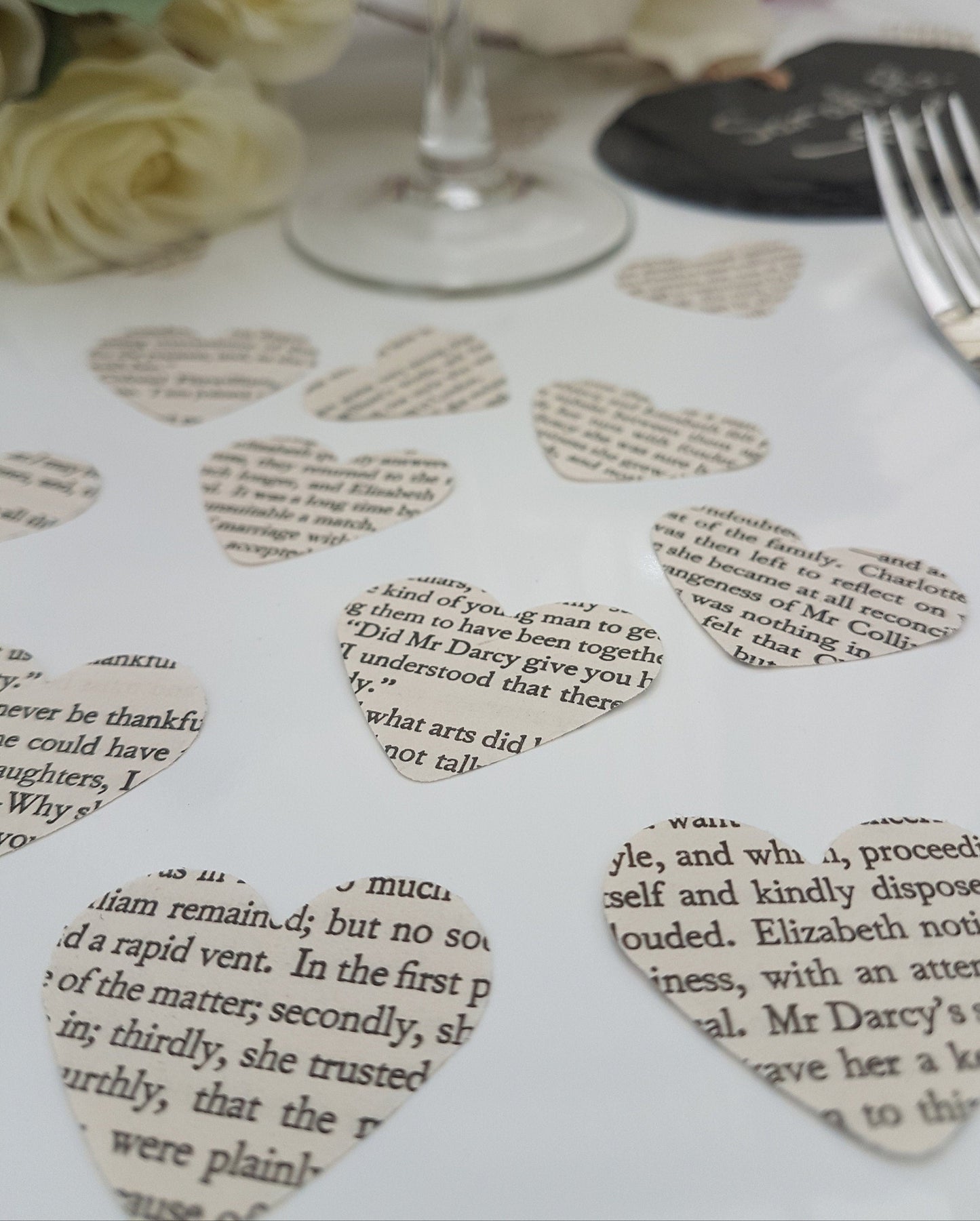Small cream paper confetti hearts are scattered on a white background. The text displayed on the confetti pieces shows text from Pride and Prejudice