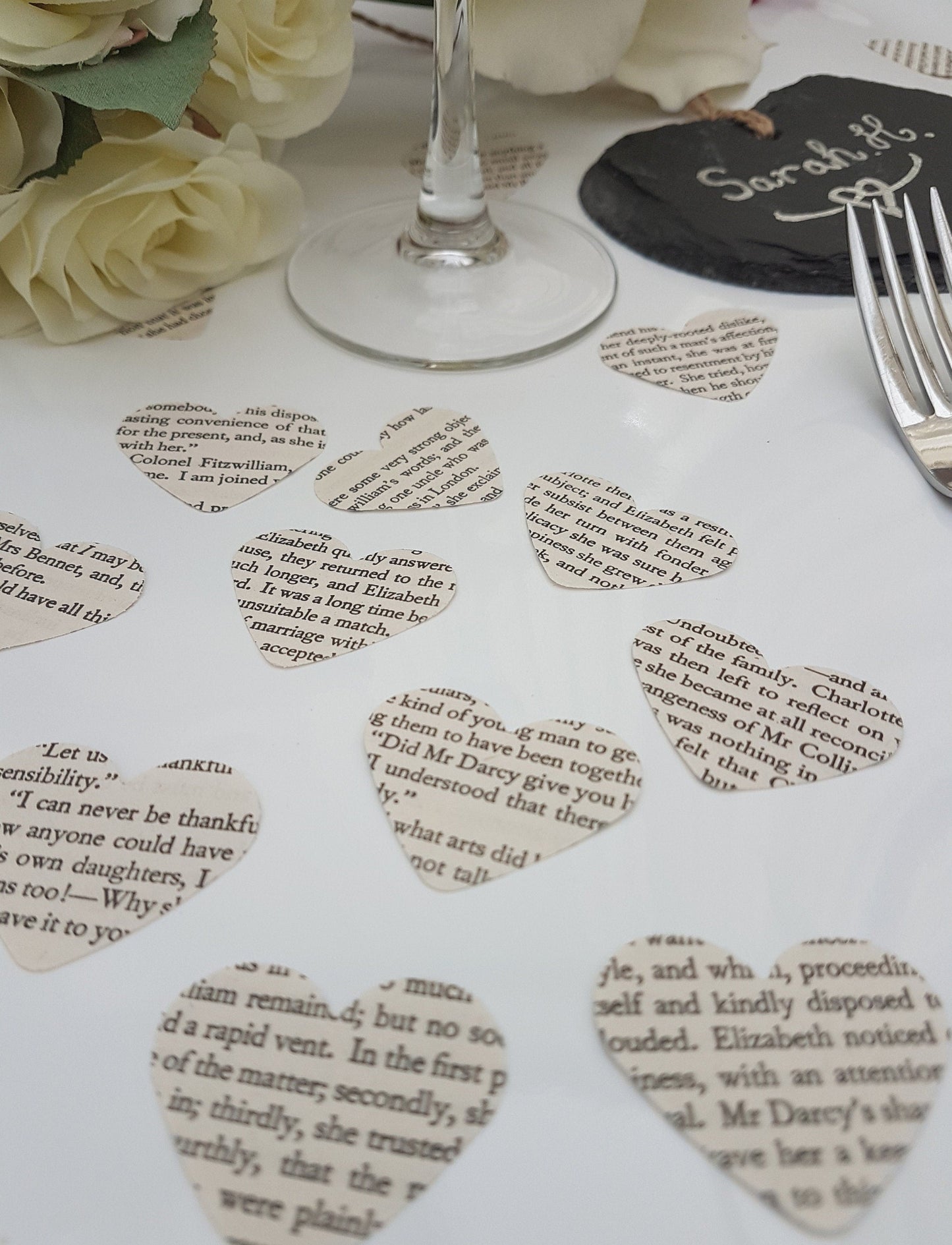 Small cream paper confetti hearts are scattered on a white background. The text displayed on the confetti pieces shows text from Pride and Prejudice