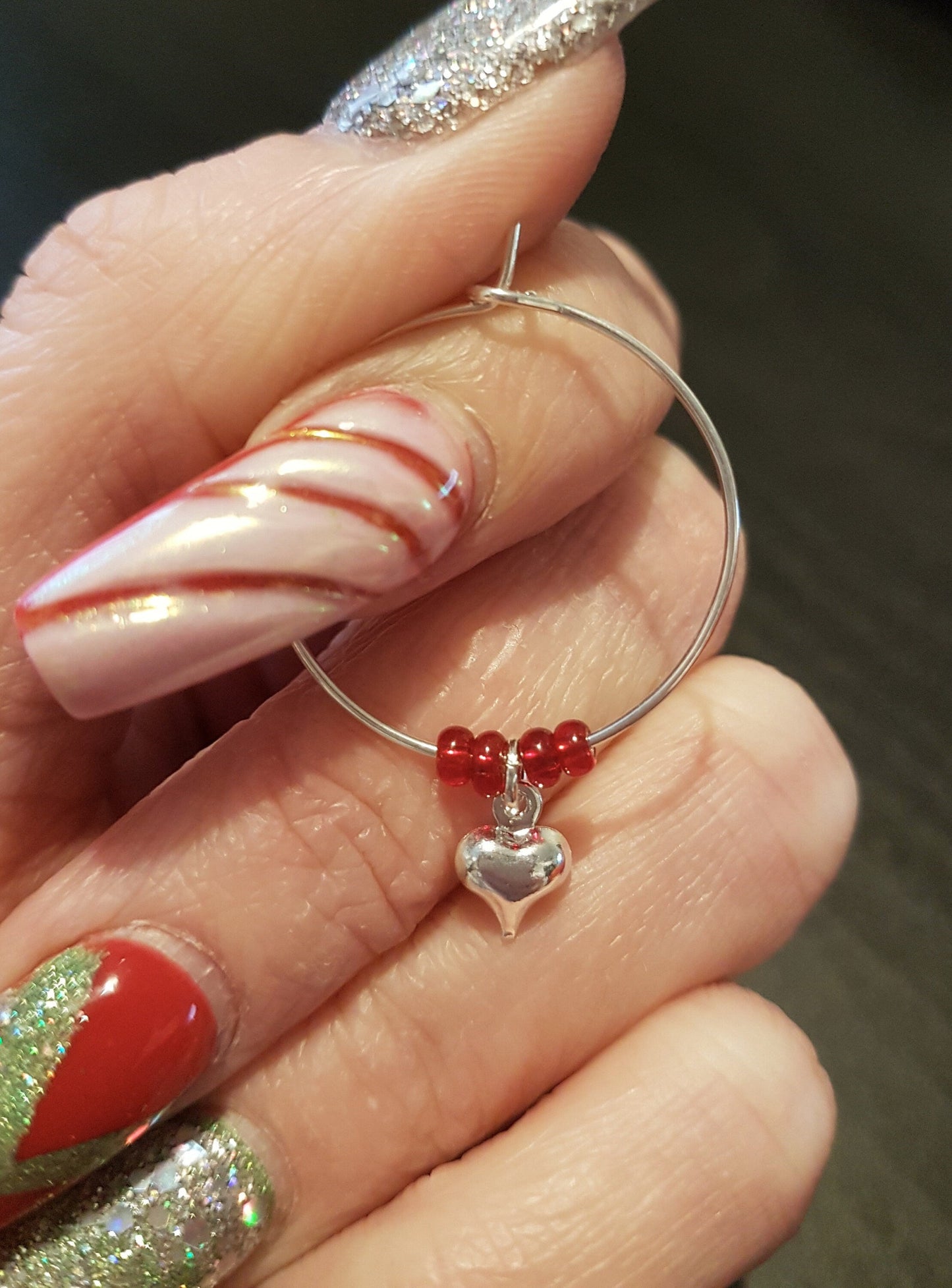 Single wine glass charm is shown held in fingers for scale. The wine charm hoop has 4 red seed beads and a silver coloured puffy heart