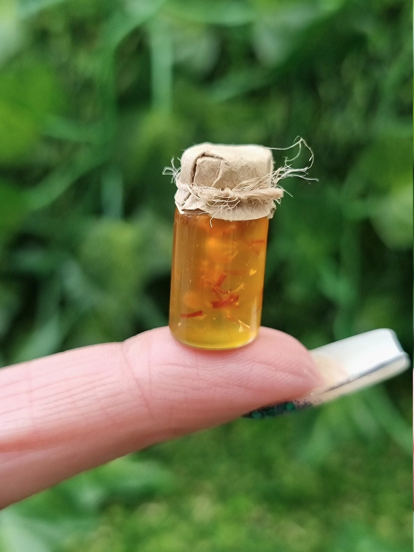 A miniature jar of shredded orange marmalade with a brown paper lid is shown on an index finger against a green background