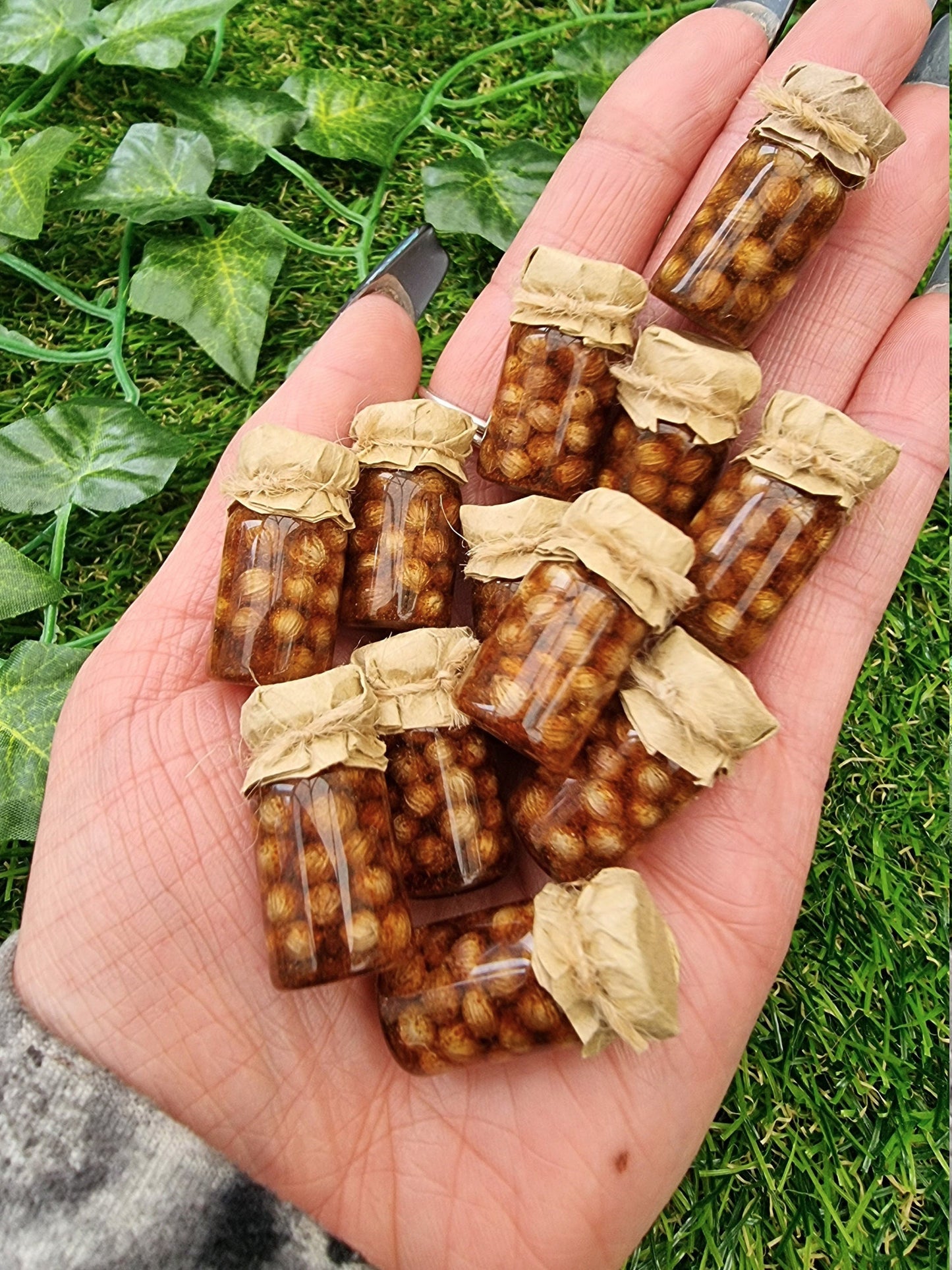 Several 1:12 scale miniature preserve jars with paper lids held in an open palm. Jars contain pickled onions
