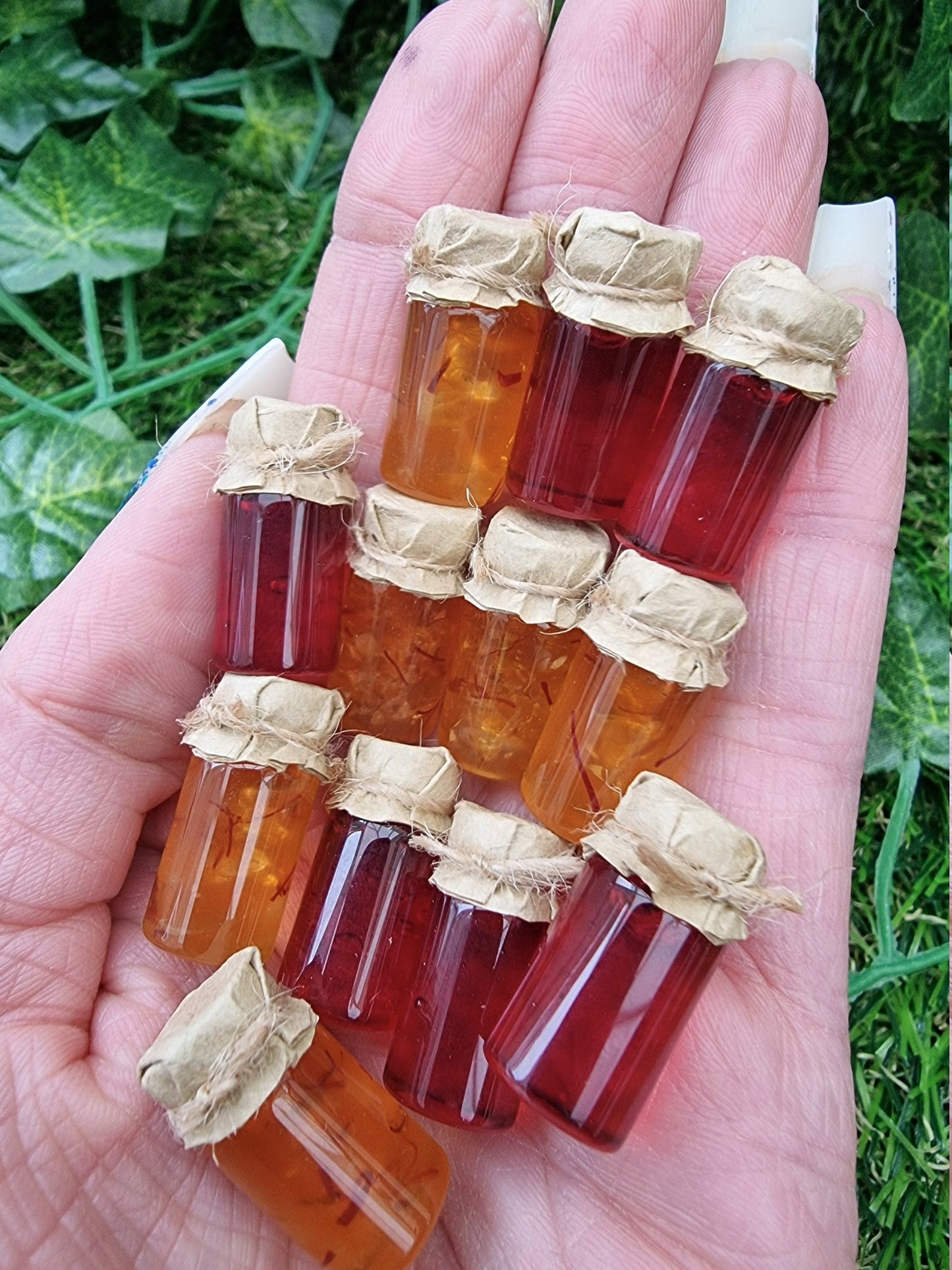 Several miniature jars of shredded orange marmalade and crimson jam with brown paper lids are show held in the palm of a hand against a green background