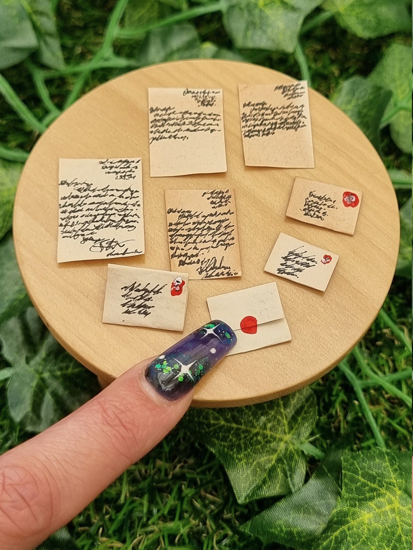 8 1:12 scale miniature aged letters are displayed on a miniature round table. 2 letters are part written, 2 are fully written, 2 are sealed letters and 2 are opened letters. A finger points to a sealed letter to show scale.