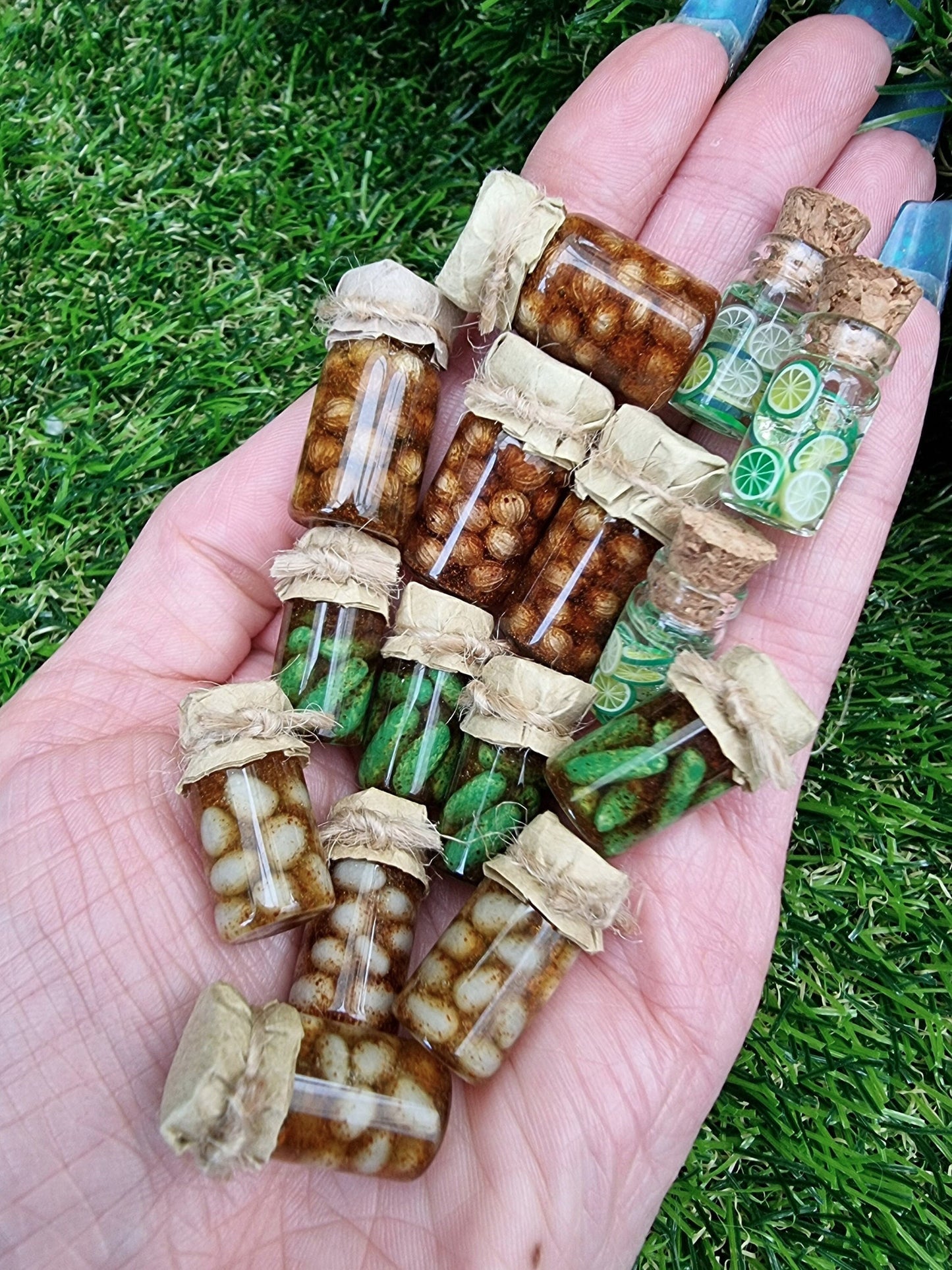 Several 1:12 scale miniature preserve jars with paper lids held in an open palm. Jars contain pickled onions, pickled eggs, gherkins and lime slices