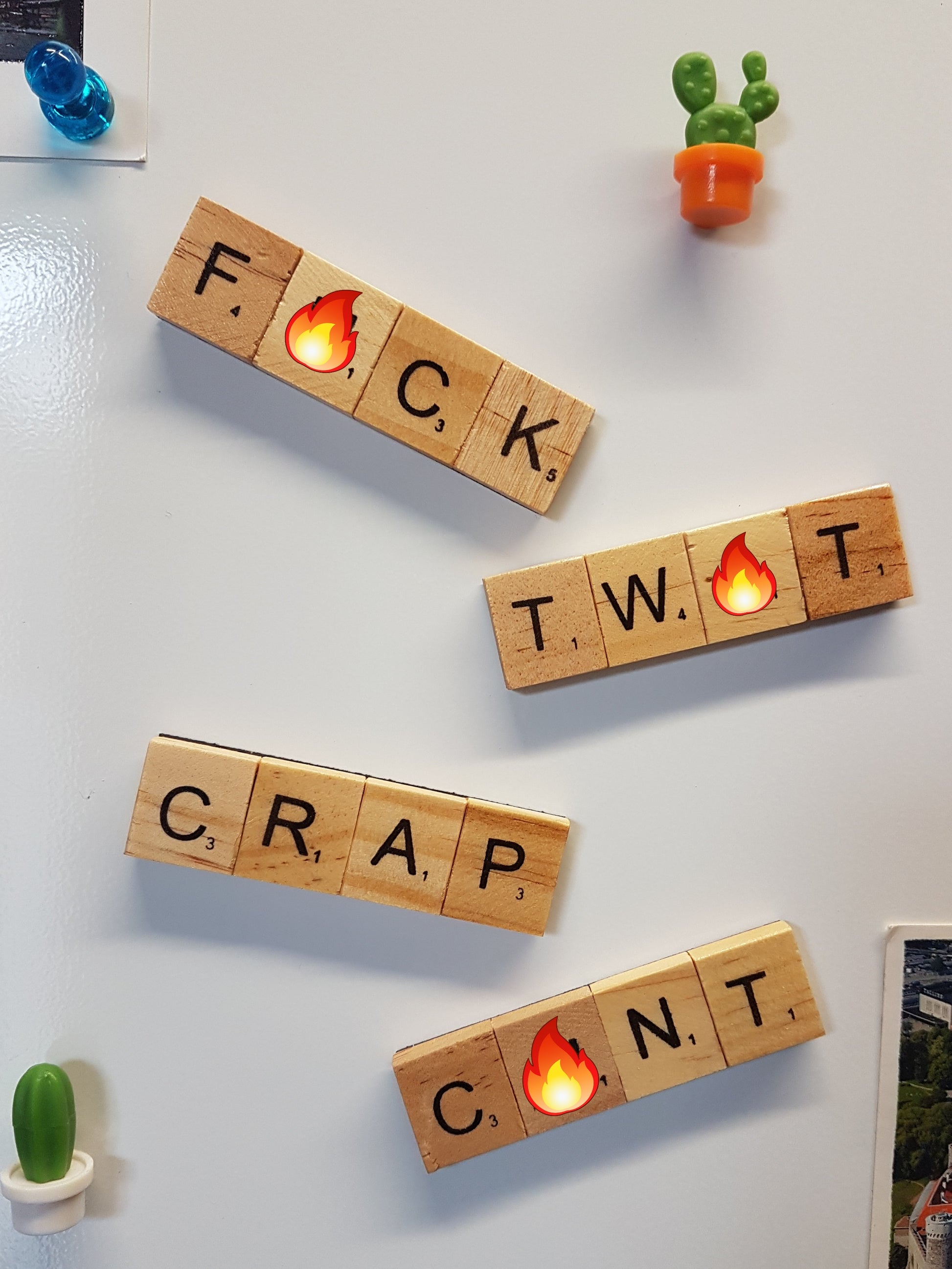 4 fridge magnets made with wooden scrabble tiles are stuck to the front of a fridge. The words spelled are swearwords, andeach swearword hasan emoji over one of the letters to read F#ck, Tw#t, Crap and C#nt