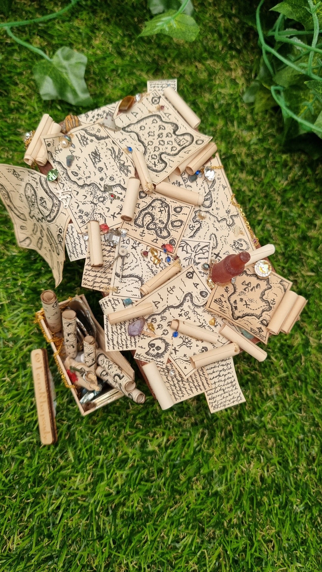 1:12 scale dollshouse brown table scattered with pirate treasure maps, bottle of rum and treasure. Wooden crate filled with treasure sits below the table