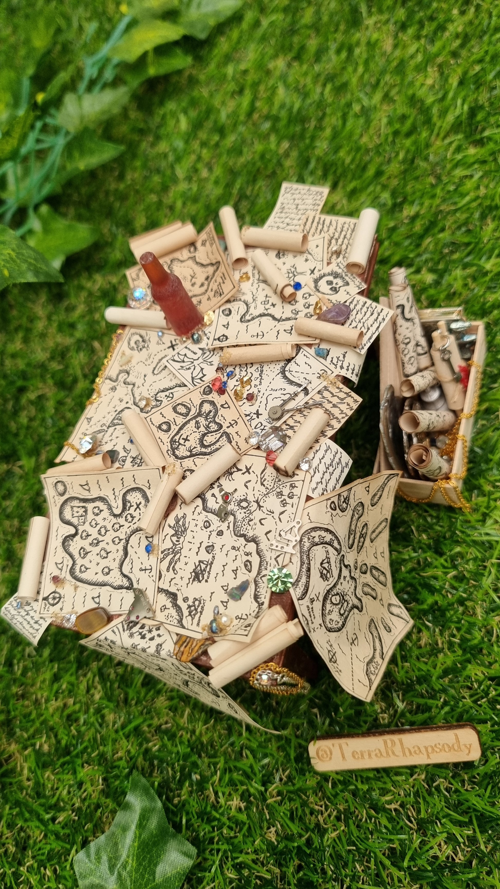 1:12 scale dollshouse brown table scattered with pirate treasure maps, bottle of rum and treasure. Wooden crate filled with treasure sits below the table and @TerraRhapsody 