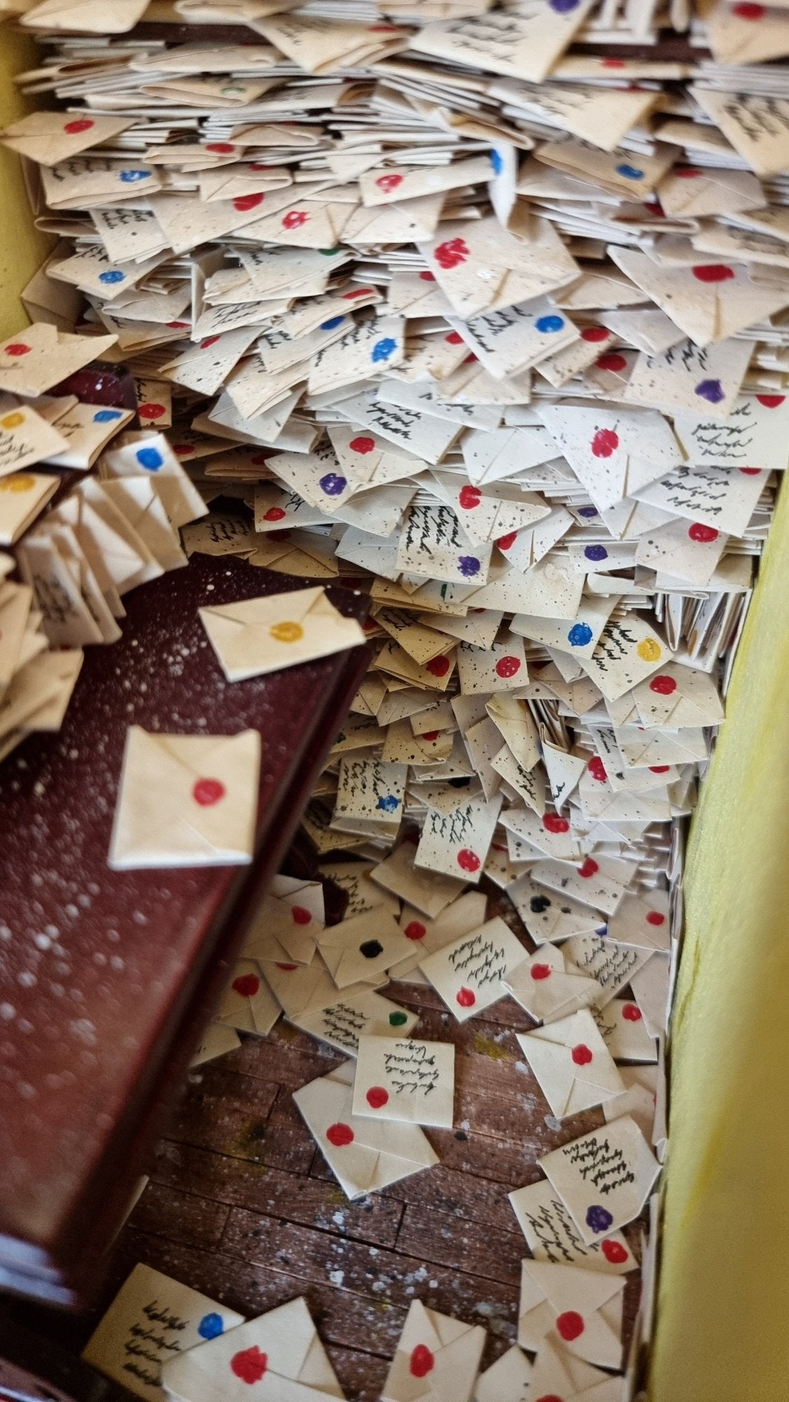 Hundreds of 1:12 scale letters are crammed into shelves above a desk crammed with more letters. The floor is also strewn with letters 