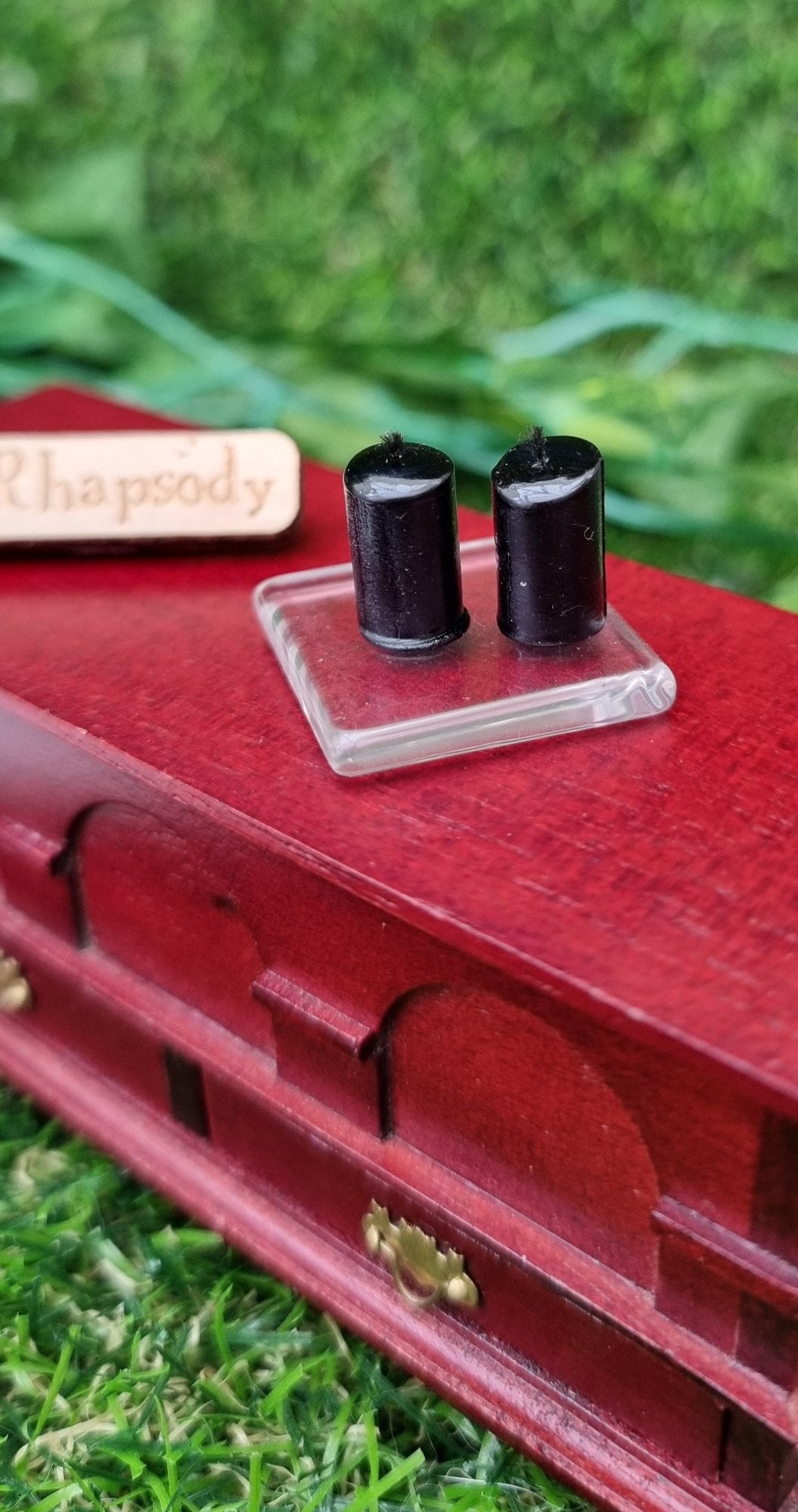 1:12 scale miniature black candles sit on a square glass plate on top of a wooden chest. There are 2 black candles on a the glass plate . @TerraRhapsody is written on wood in the background