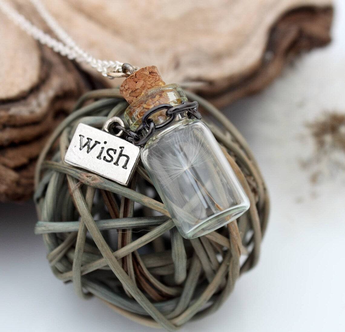 Miniature jar shaped glass vial necklace containing a dandelion seed with a silver coloured wish charm hung on black chain around thr neck of the jar. Displayed a silver coloured chain attached to a cork lid