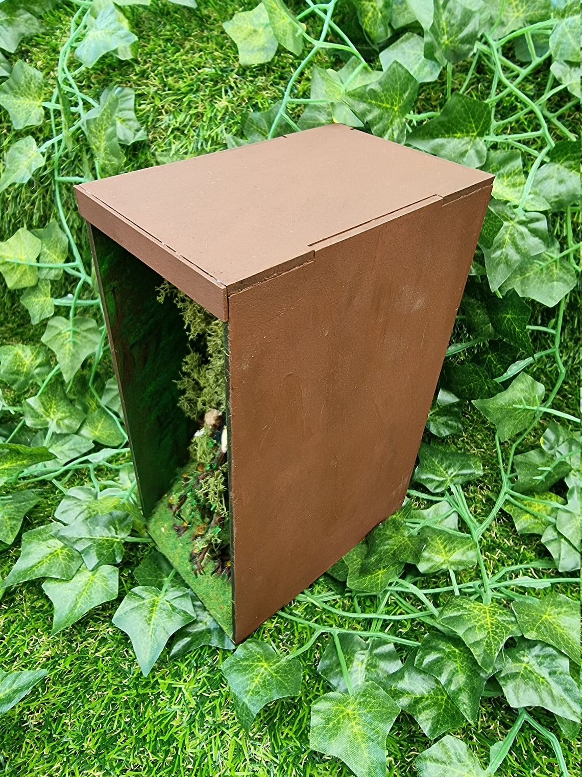 View shows the top of the brown book nook box against a green ivy background. The front of the book nook box scene can be seen with trees and hobbit visible