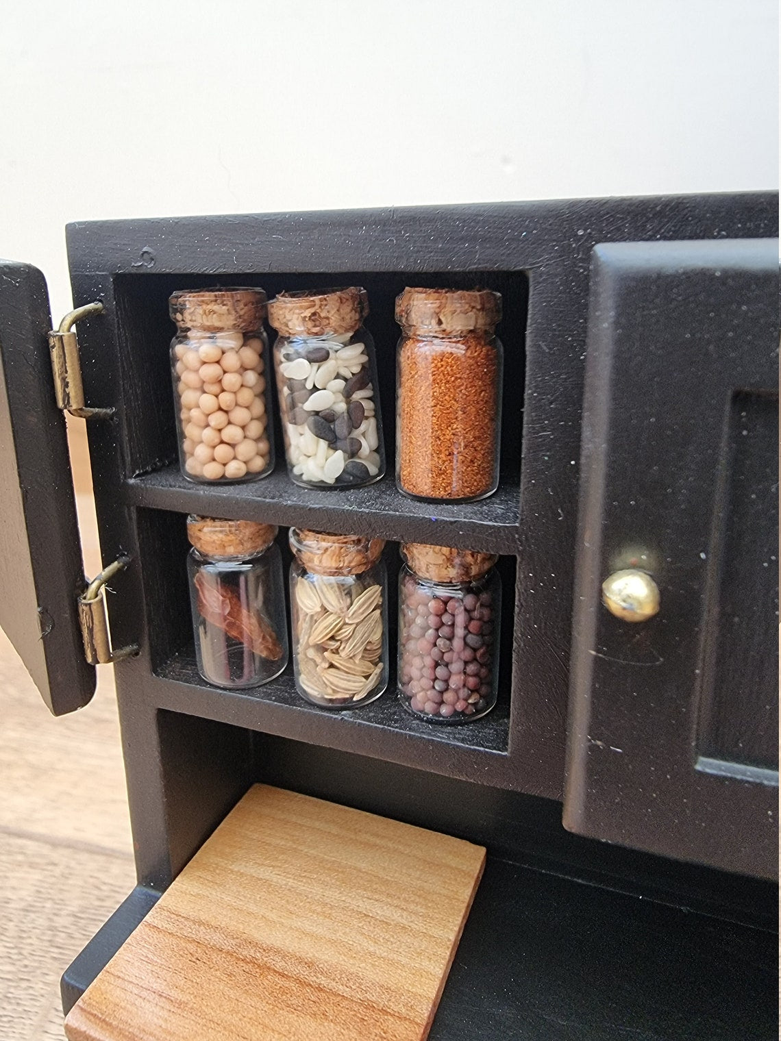 Set of 1:12 scale miniature apothecary jars with cork lids displayed in a black cupboard. Jars contain different herbs and spices