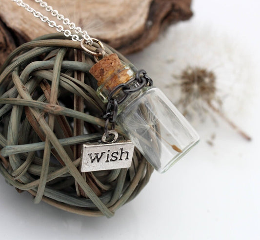 Miniature jar shaped glass vial necklace containing a dandelion seed with a silver coloured wish charm hung on a black chain around the neck of the jar. Displayed on a silver coloured chain attached to the cork lid