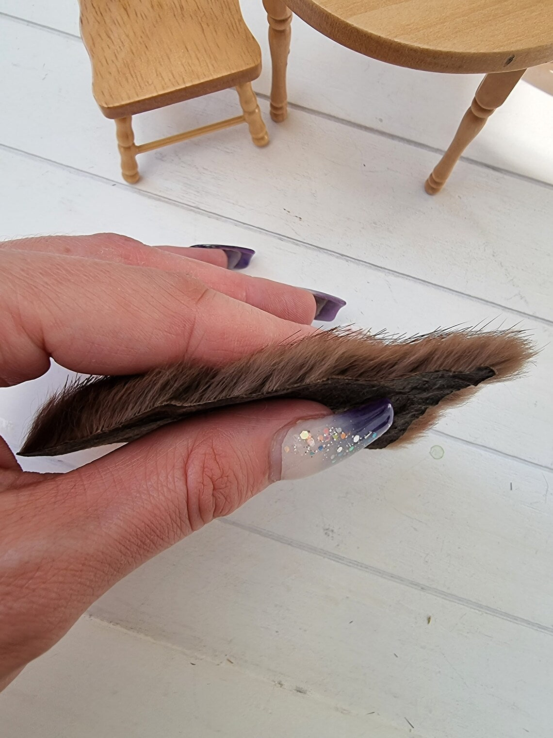 Hand holds a dark brown 1:12 scale animal skin genuine fur rug to show the depth of the rug pile. The rug appears thick, but the hair is fine, so it flattens down