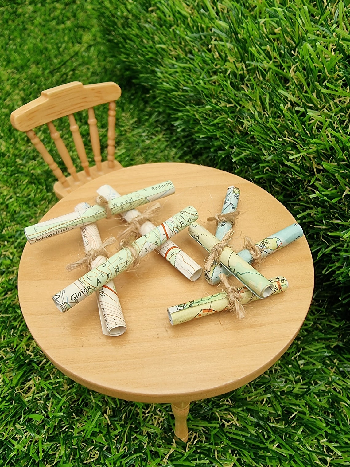 1:12 scale Miniature map scrolls tied with jute string are displayed on a miniature wooden table. The maps are mainly coloured white, green and blue