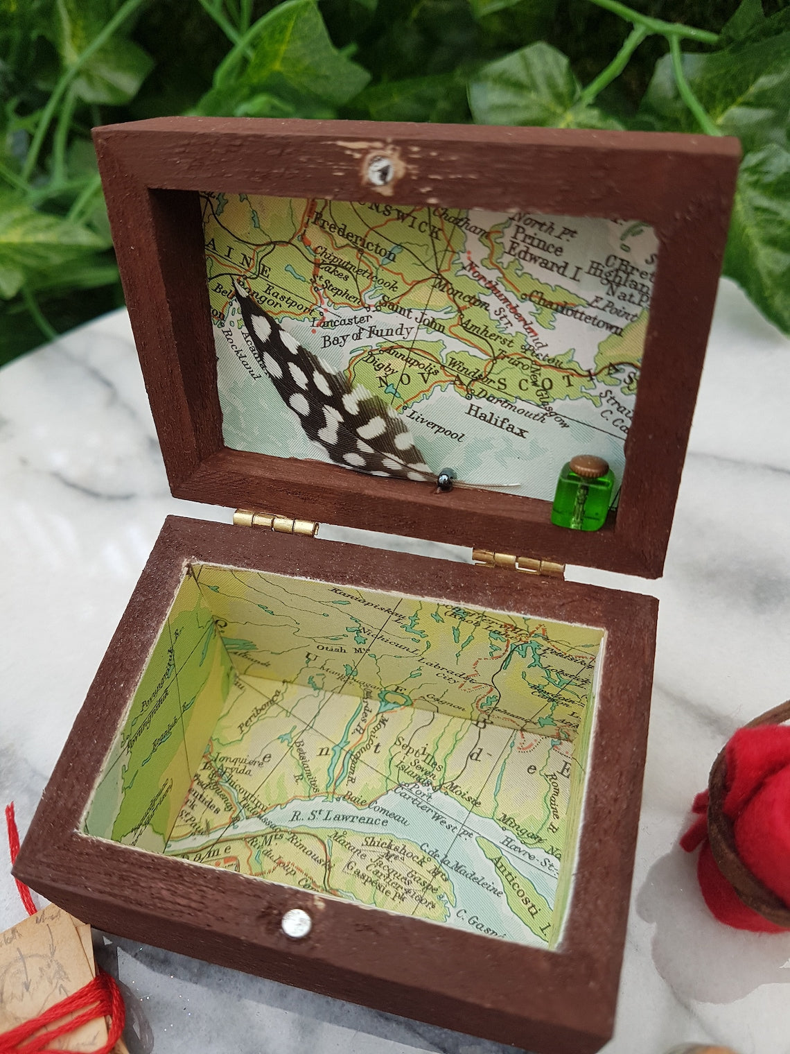 An empty, open travellers chest is shown with a green glass inkwell and feather quill. The inside of the chest is lined with coloured map paper