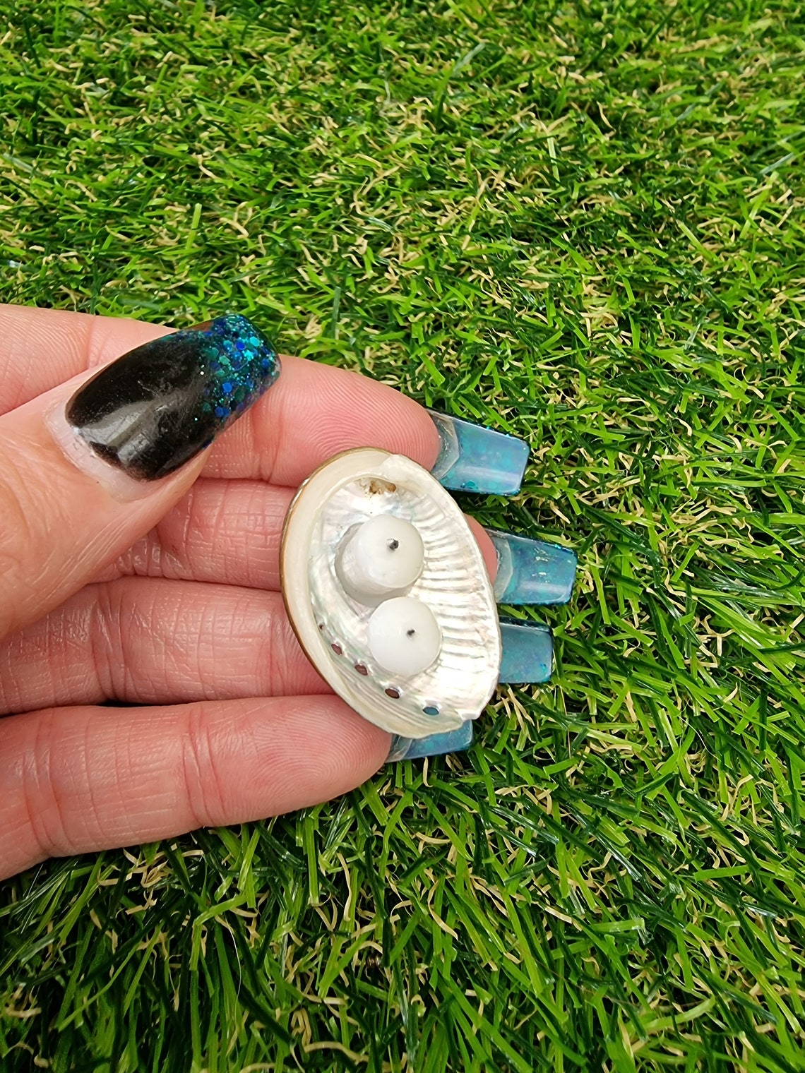 View from above of Two white 1:12 scale miniature candles in a small abalone shell dish. Displayed on fingers of an open hand