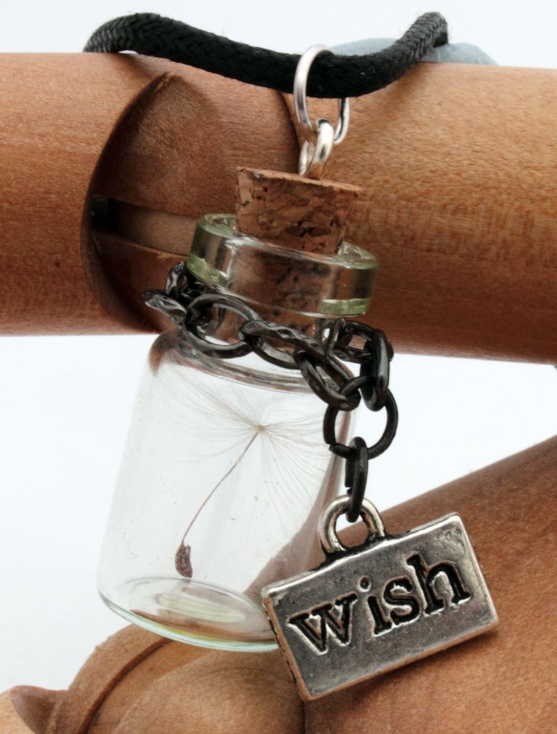 Miniature jar shaped glass vial necklace containing a dandelion seed with a silver coloured wish charm hung on black chain around the neck of the jar. Displayed a silver coloured chain attached to a cork lid