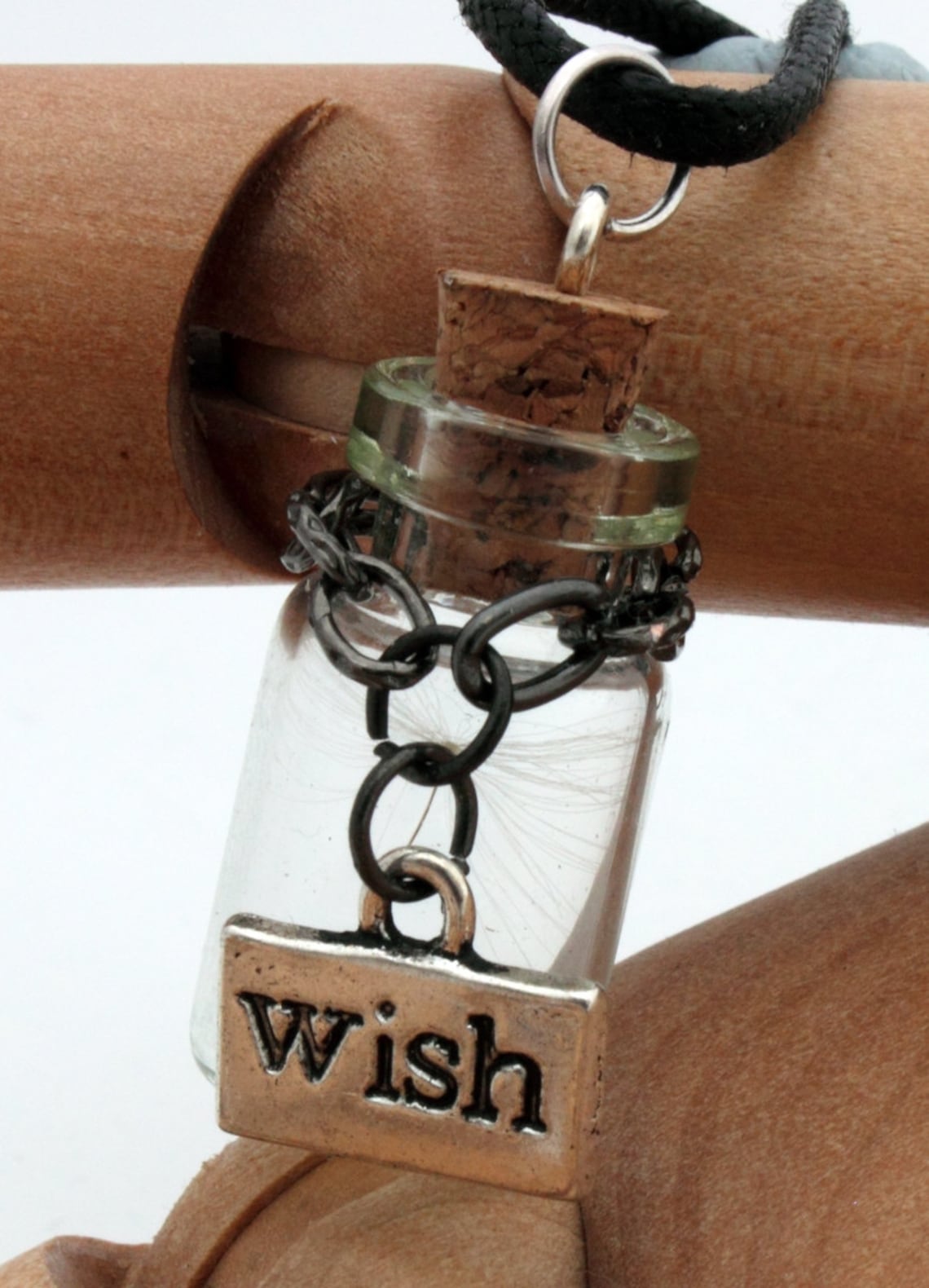 Miniature jar shaped glass vial containing a dandelion seed with a silver coloured wish charm hung on black chain around the neck of the jar. Displayed a black coloured cord attached to a cork lid