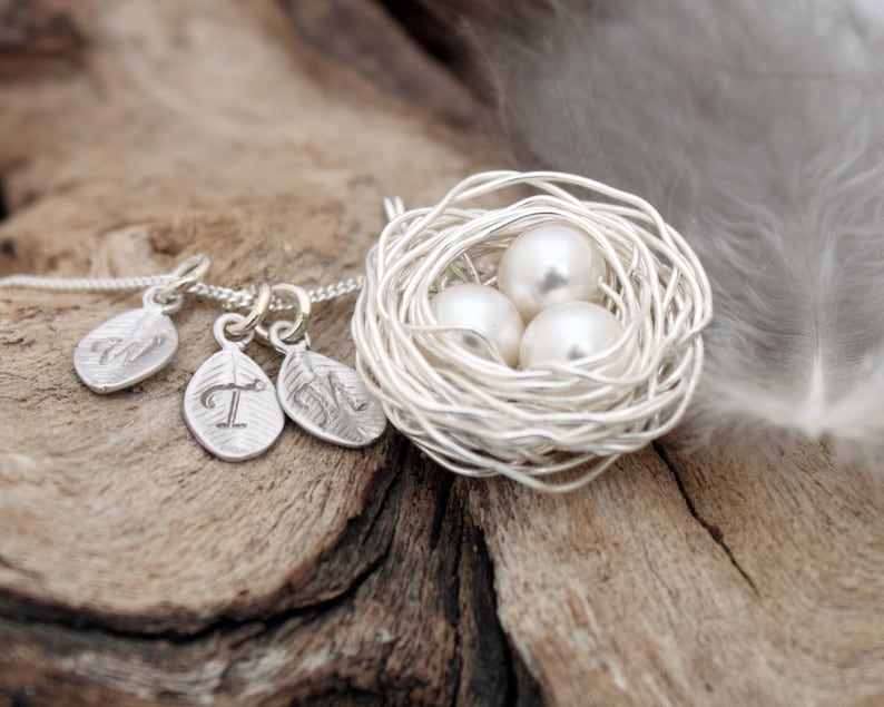 Silver coloured woven wire and ivory pearl eggs necklace with 3 silver coloured leaf charm with stamped calligraphic initials V, T and M on the silver chain