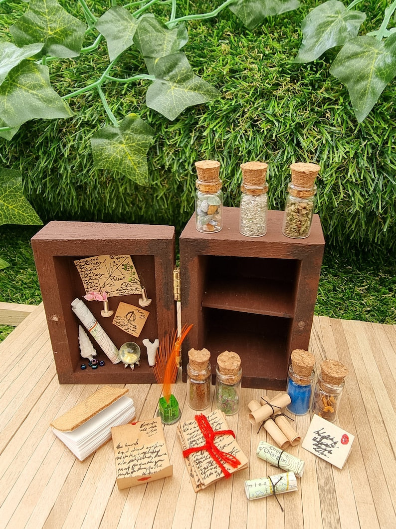 A 1:12 scale miniature brown apothecary cabinet shown open. The contents sit in front: glass vials, parchment scrolls, letters, notes, inkwell and quill. The left cabinet door has aged notes pinned up, shells, crystal ball, map, coral and slim vases