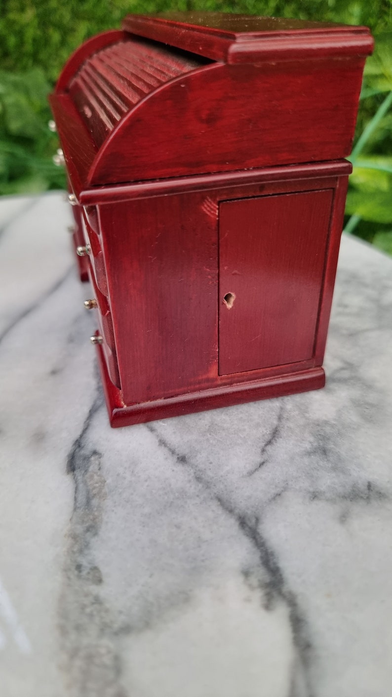 Side view of a 1:12 scale brown rolltop desk showing a cupboard with a keyhole in the side of the desk. There are scratches on the top left corner above the cupboard door