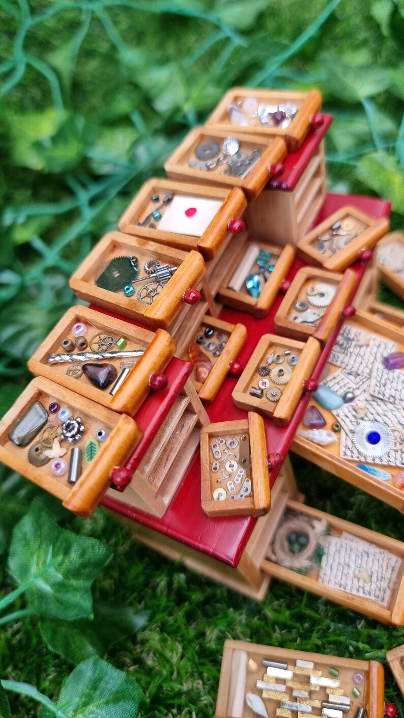 Detail of a 1:12 scale desk with 21 drawers has all drawers removed and on display. Each drawer is filled with different items, including parchments, shells,  letters, quill, gemstones, nest, trinkets and curios