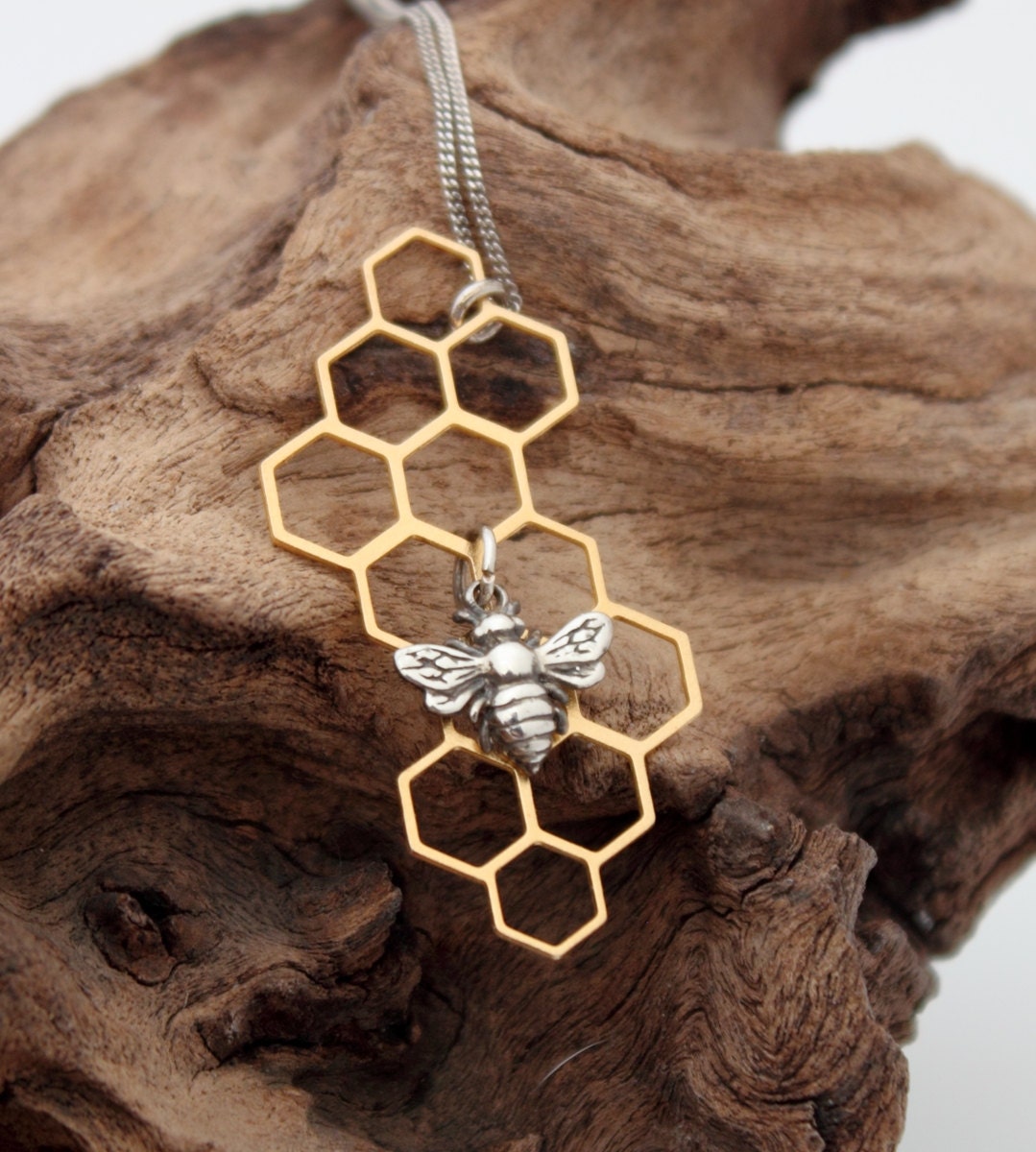 A sterling silver bee charm hangs from the centre of a brass geometric filigree honeycomb piece. The silver bee compliments the golden brass. The geometric honeycomb hangs on a fine silver chain.