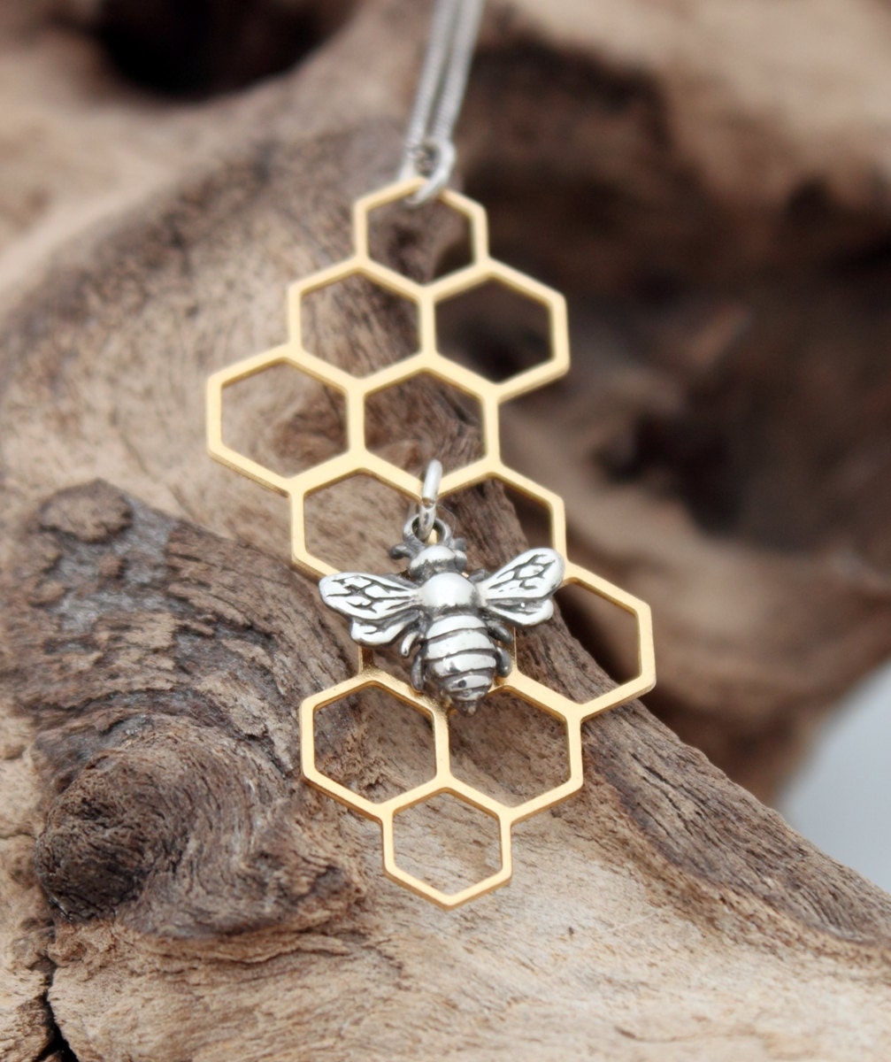 A sterling silver bee charm hangs from the centre of a brass geometric filigree honeycomb piece. The silver bee compliments the golden brass. The geometric honeycomb hangs on a fine silver chain.