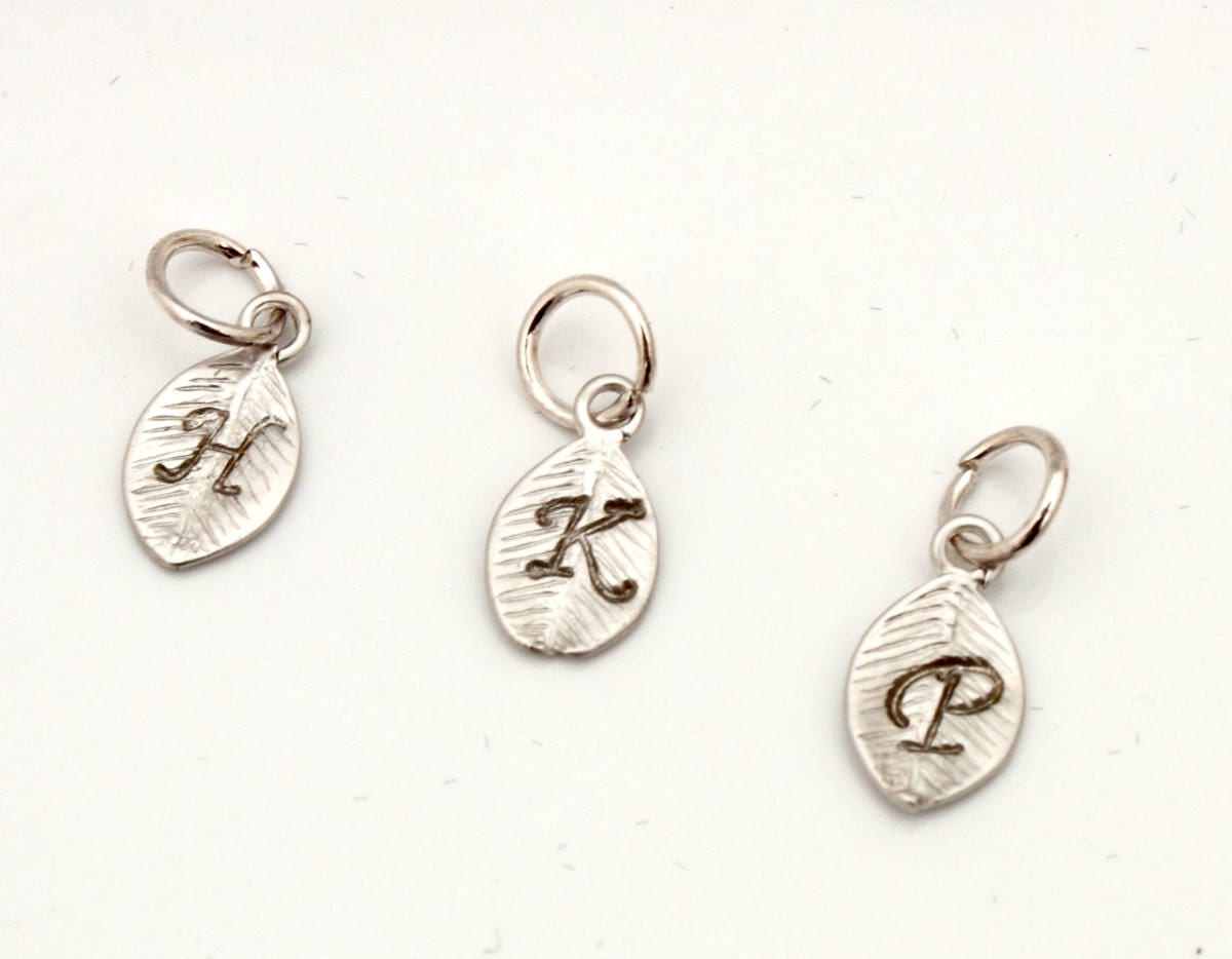 3 metal leaf-shaped charms with a small loop and jump ring on a white background. The charms are silver coloured with a stamped calligraphic initials H, K and P