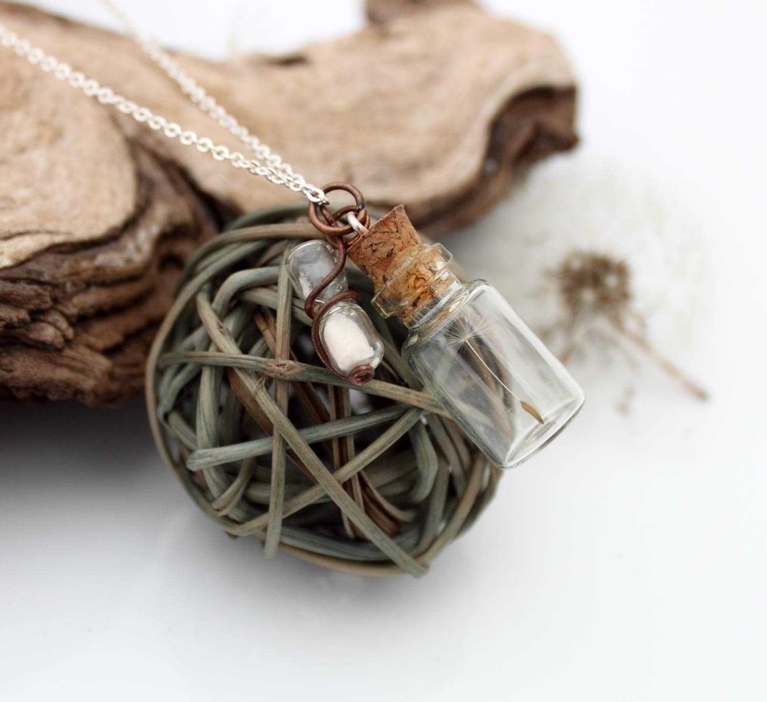 Miniature jar shaped glass vial necklacecontaining a dandelion seed with a copper wrapped miniature glass sand timer attachdd to the cork lid. Displayed on a silver coloured chain attached to the cork lid