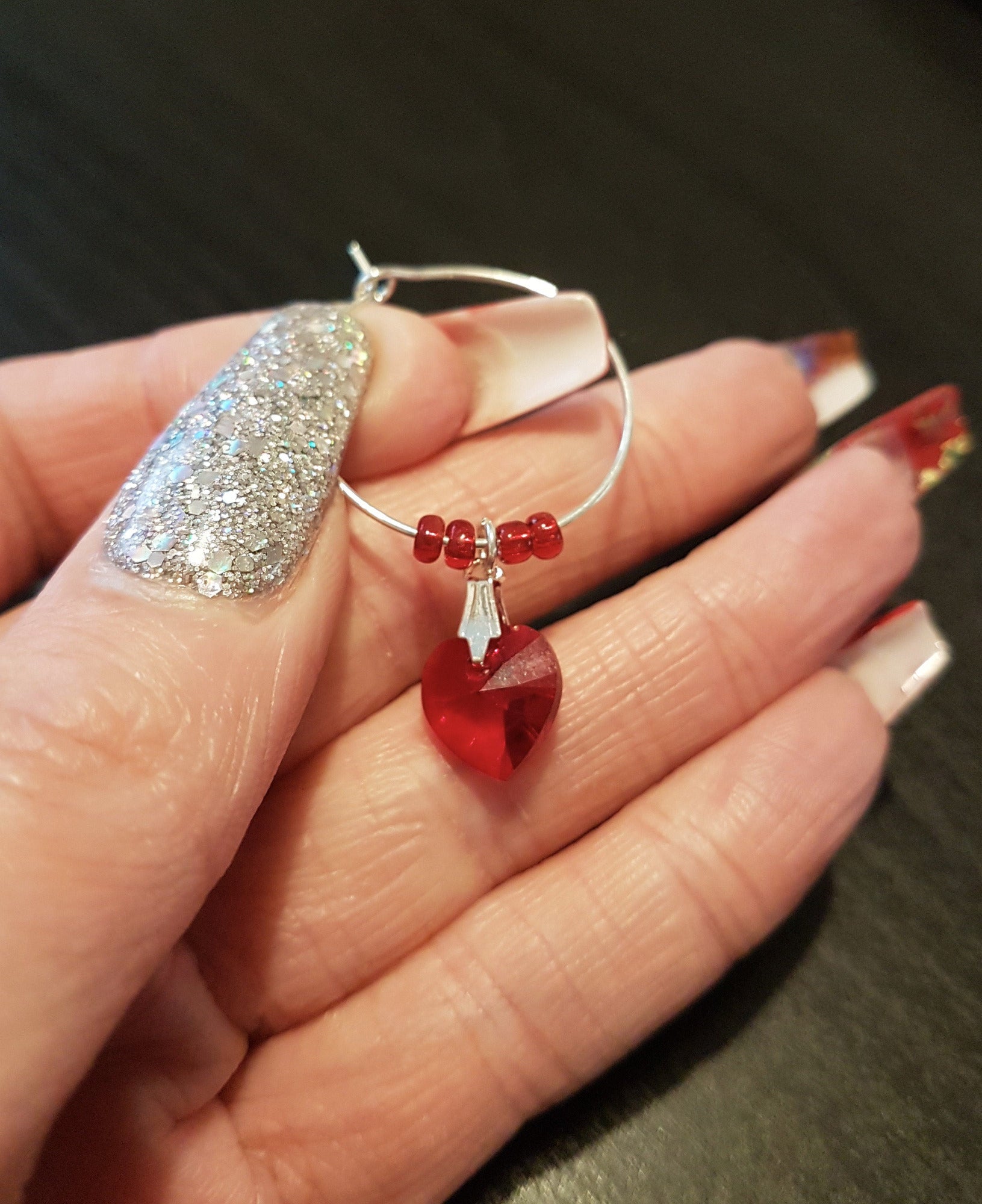 A single wine glass charm is shown held on fingers with red seed beads and a red swarovski crystal heart dangling down