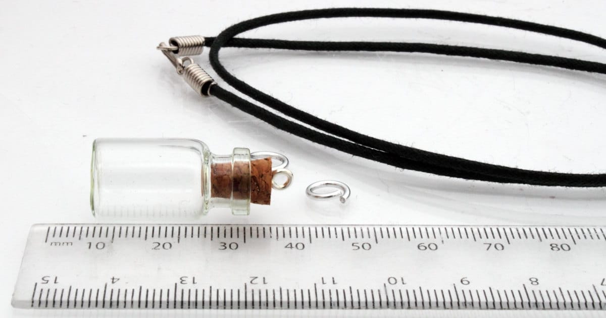 Medium jar glass vial with a cork bung sits beside a ruler, jump rings and a black pendant cord 