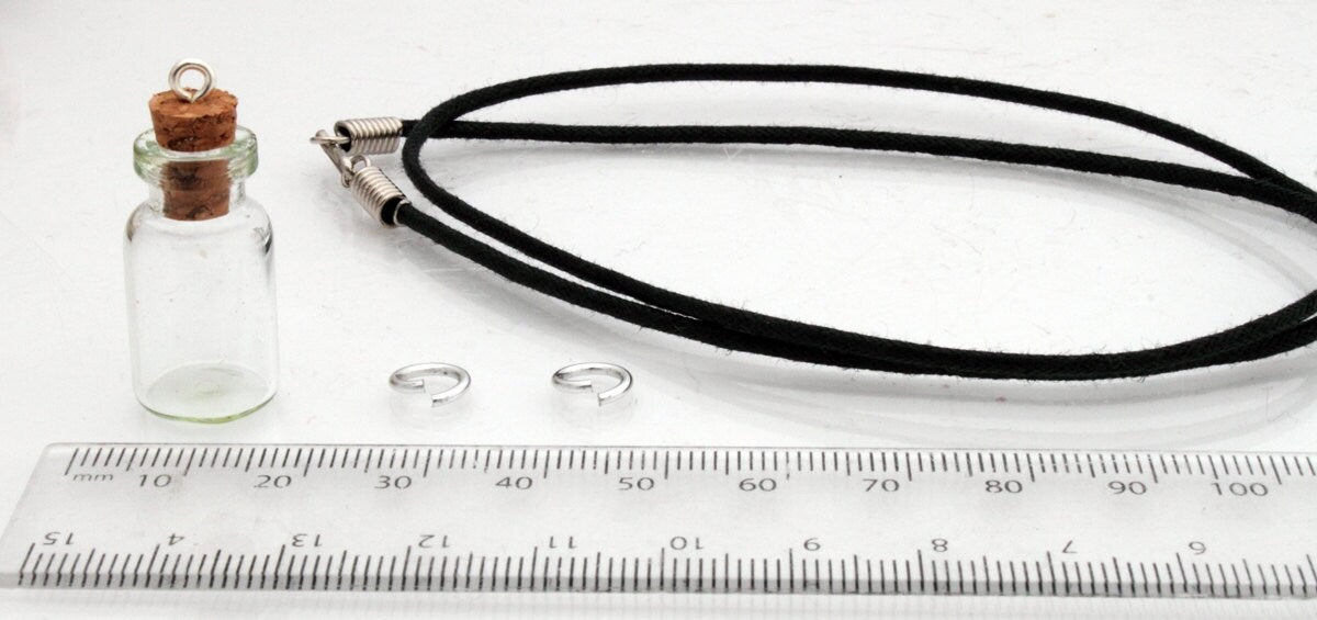 Medium jar glass vial with a cork bung sits beside a ruler, jump rings and a black pendant cord 